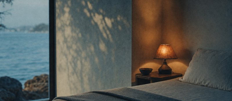 Bettecke mit gefalteter Wolldecke und einer niedrigen Nachttischlampe (mit AI erstelltes Bild)