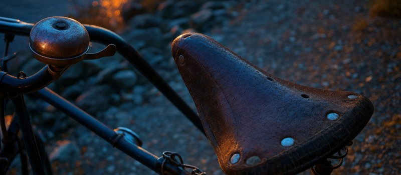 Fahrradklingel und abgenutzter Ledersattel in Nahaufnahme über einem Schotterweg (mit AI erstelltes Bild)